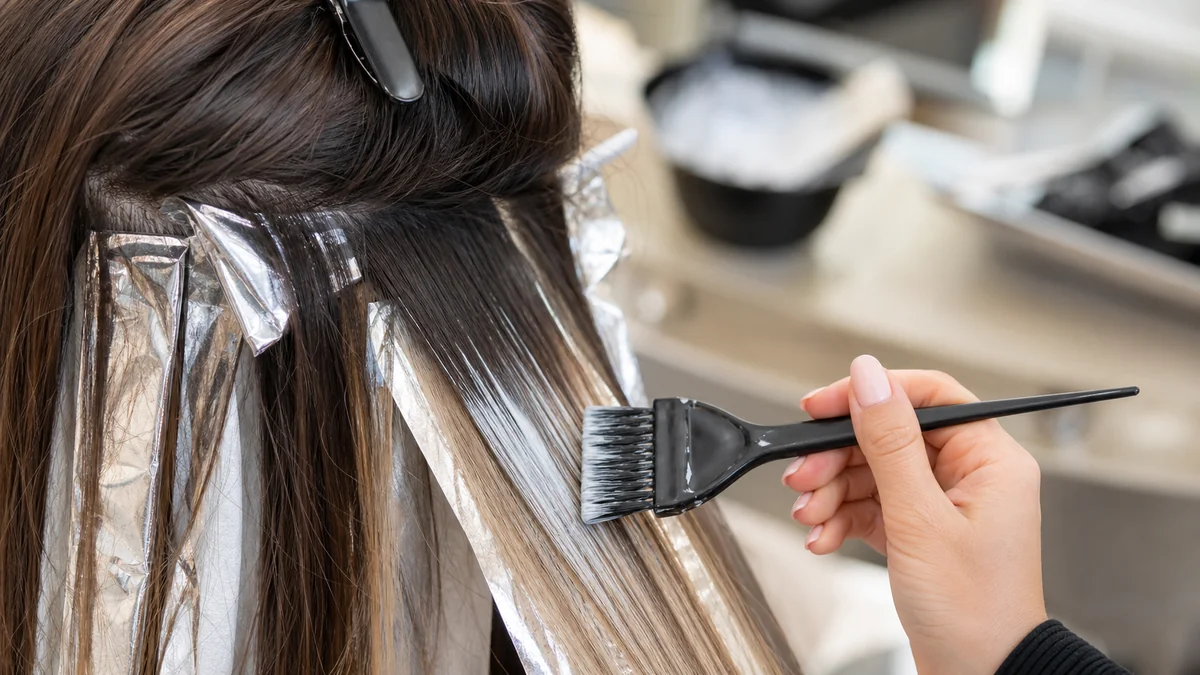 Stylist applying lightener to brunette hair for a soft balayage effect