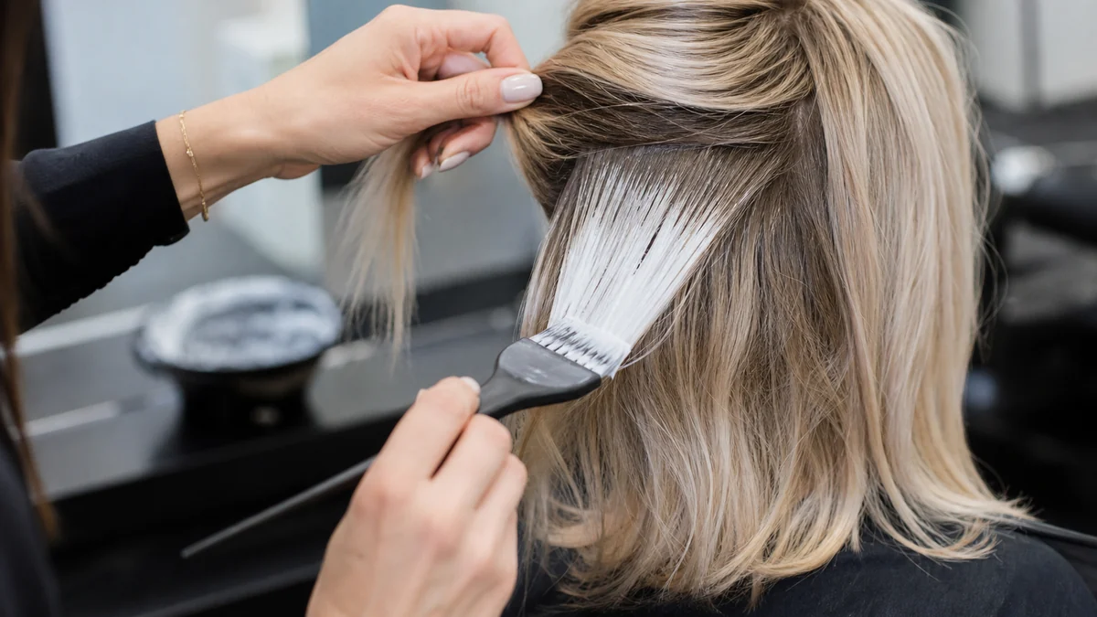 Colorist hand-painting lightener onto sectioned blonde hair